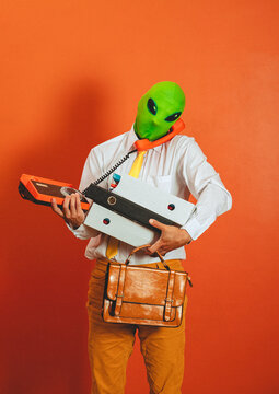 Overwhelmed man in alien mask holds retro telephone and binder