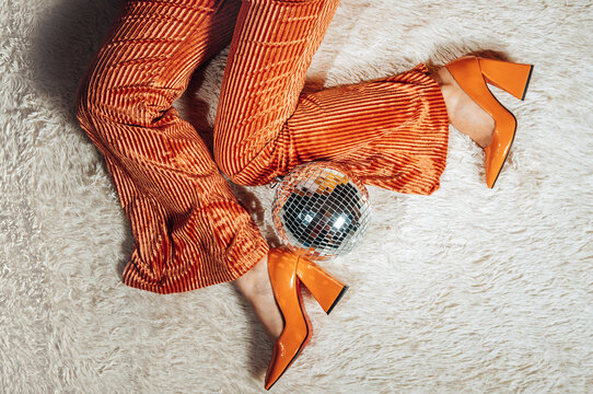 Woman wears orange retro pants and shoes near a disco ball