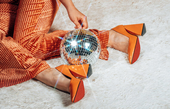 Woman in orange bell-bottom pants touches a disco ball on a carpet