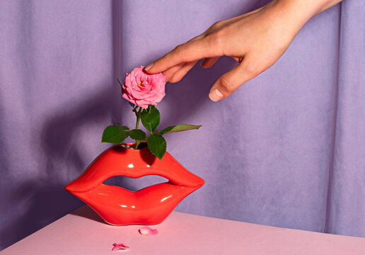 Female hand touching a pink rose in a red lip vase indoors