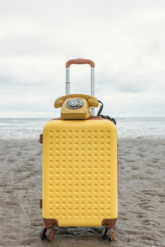 Yellow suitcase and vintage telephone sit on a sandy beach