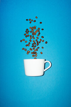 A white coffee cup catches falling coffee bean on blue background