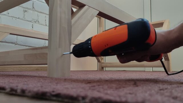Person assembling wooden furniture with an electric screwdriver on the floor