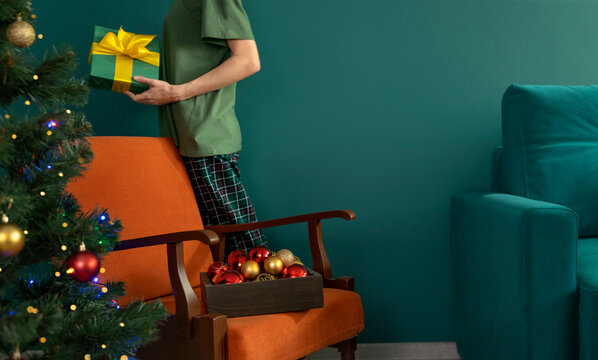 Woman holds a wrapped Christmas present near an armchair at home