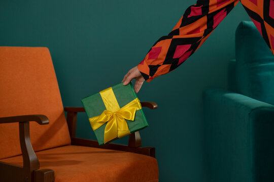 Woman puts a wrapped gift on an orange armchair indoors