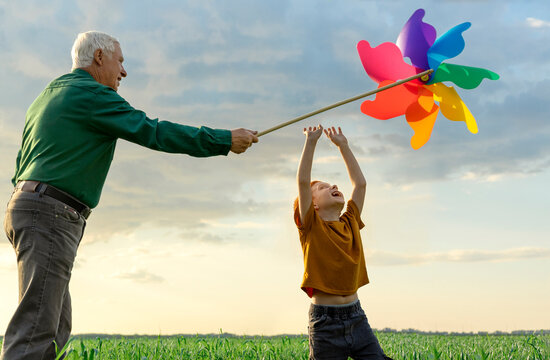Grandfather and grandson play with a colorful pinwheel in the field