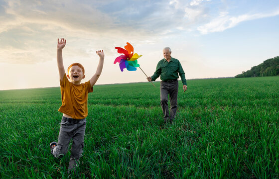 Grandson runs in a field while grandfather walks with a chopper