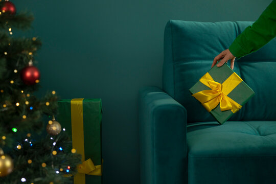 Woman places a wrapped Christmas gift on a green sofa at home