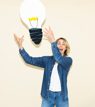 Excited woman catches a paper lightbulb indoors for a creative idea