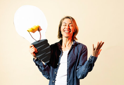 Smiling woman holds a paper lightbulb indoors to show creativity