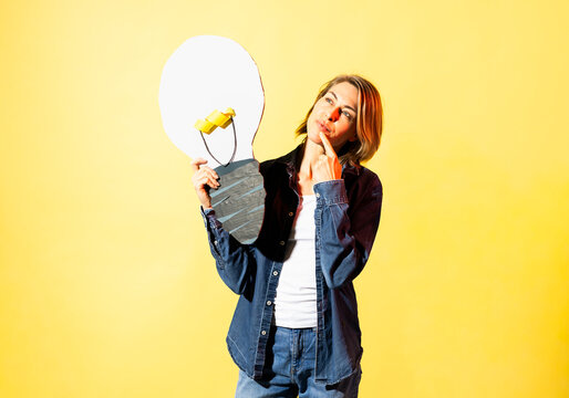 Thoughtful woman holds a paper lightbulb indoors