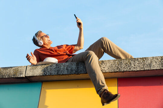 A happy man uses a smartphone while lying on a wall in Barcelona