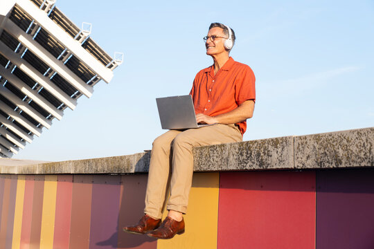 Man sits on a colorful wall in Barcelona and works on a laptop