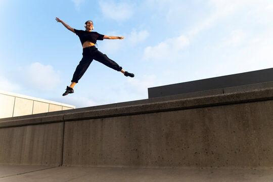 Woman jumps energetically over concrete wall outdoors in Barcelona