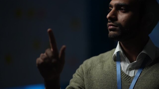 A bearded engineer raising one finger marks a point mid sentence in a low key portrait against the dark inside a dimly lit artificial intelligence startup office at night.
