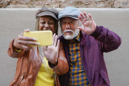 Happy multiracial senior couple using smartphone for video call with family during city trip - Autumn season, joyful elderly people, technology and travel concept