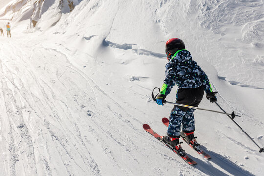 Scenic back view kid beginner skier close-up downhill start line rows freshly prepared groomed ski slope piste bright warm morning sunrise sky background. mountain landscape winter resor
