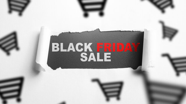 Black Friday sale concept showing the promotional text revealed through torn paper, surrounded by blurred shopping cart icons