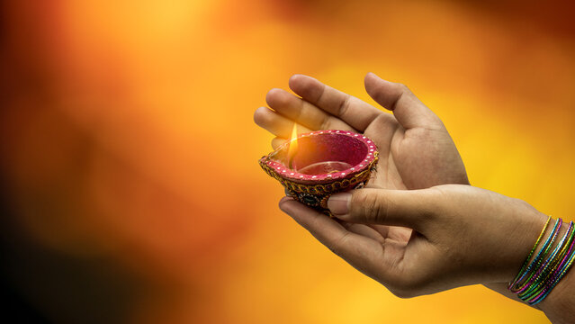 Hands holding a decorated burning clay diya against a warm golden background, celebrating Diwali, the Indian festival of lights. Diwali festival celebration