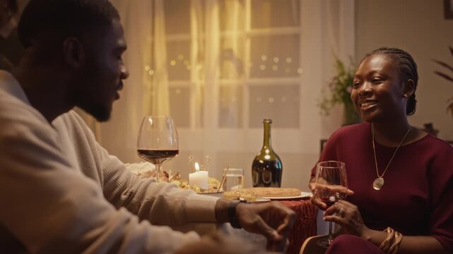 African American young adults talking and drinking red wine during Thanksgiving dinner celebration at table. Visual suitable for holiday advertising, relationship storytelling, or lifestyle promo