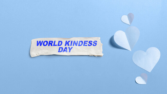 World Kindness Day written on a torn paper strip surrounded by paper hearts on a light blue textured background. Concept of World Kindness Day