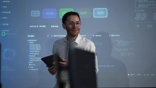 An engineer with an open palm raised invites a question mid presentation, the agent workflow still running on the screen behind him inside a dark AI startup office.