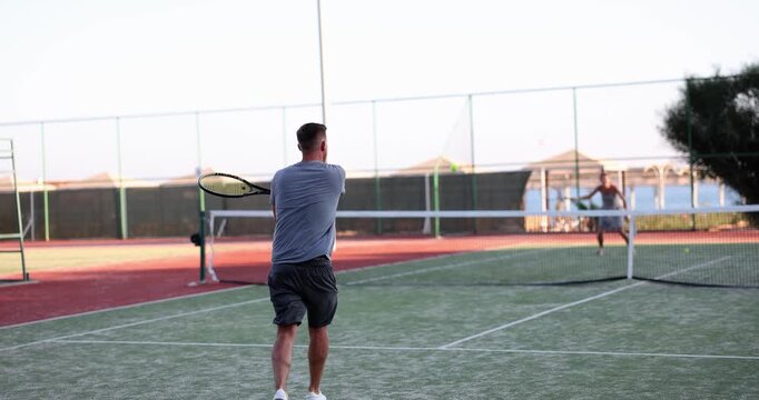 Players engage in an exciting tennis practice under a clear blue sky. The vibrant green court sets a lively backdrop for their spirited training.