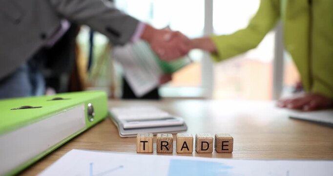 In a lively office filled with papers and ideas, two professionals exchange a firm handshake, marking the beginning of a promising partnership focused on trade.