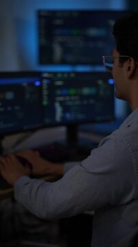 An engineer at a wall of blurred blue screens reaches for the keyboard as the code display stretches out of focus in front of him inside a dark AI startup office.