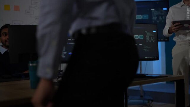 An engineer pushing back from his desk stands up mid frame and leaves the monitors still running the agent pipeline behind him inside a dimly lit machine learning startup office.