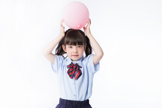 Young girl balancing pink balloon on head in school uniform