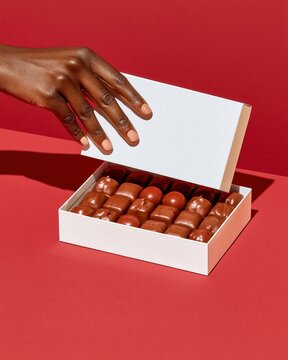 Hand opening white box of assorted chocolates on red background