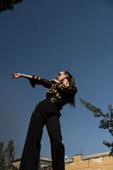 Fototapeta premium Portrait of attractive young caucasian woman wearing a yellow and black striped blouse, sunglasses and trousers posing against of a blue sky. Style, fashion, beauty.