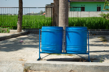 Obraz premium Blue Public Trash Bins in Rural Park Area with Green Rice Field Background