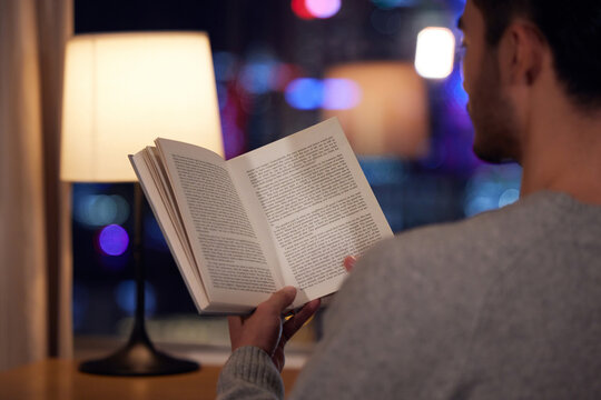Man reading book by lamp at night