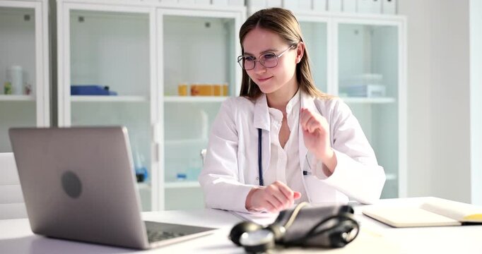In a bright clinic, a smiling healthcare professional connects with patients through a computer screen, waving and communicating warmly during online consultations, creating a welcoming atmosphere.