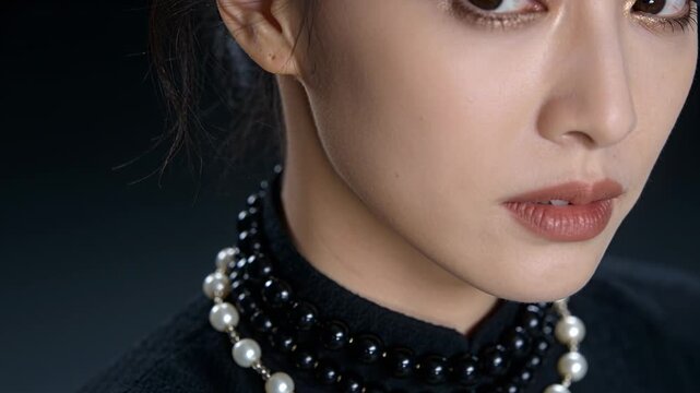 Reacting to camera model in high-neck top tilting head, lowering gaze in studio, pearls