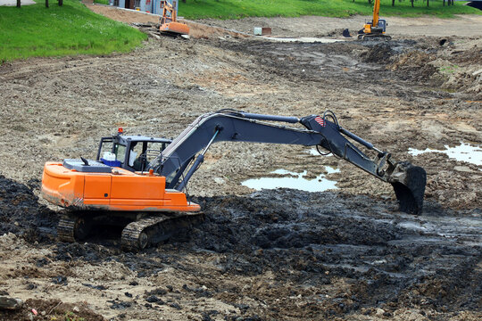 Heavy excavator operates on muddy construction site amid earthworks