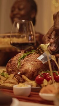 Vertical shot of African American man slicing roasted festive turkey during holiday dinner. Footage suits Thanksgiving advertising, autumn culinary promotions, and festive campaigns