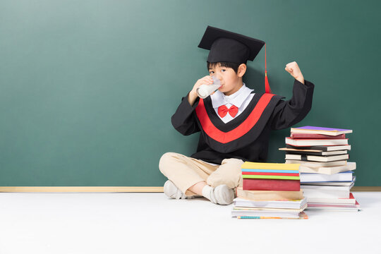 Little Boy in Graduation Cap Drinks Milk with Books