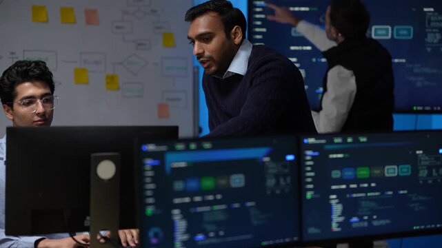 A team spread between desk and display works the architecture from both sides of the room in a long continuous take inside a dimly lit machine learning startup office.