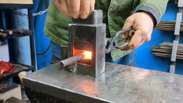 Blacksmith uses tongs to place glowing hot metal rod into custom steel die mold on industrial workshop anvil surface