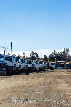 A row of large white industrial trucks is parked on a dirt lot in Angol, Chile