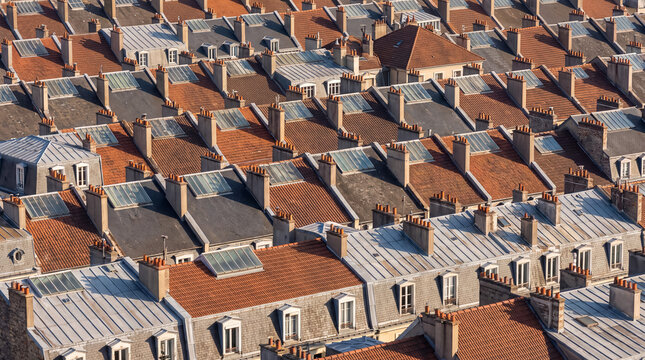 Rooftops cityscape with dense urban residential buildings, chimneys, and dormer windows under warm sunlight