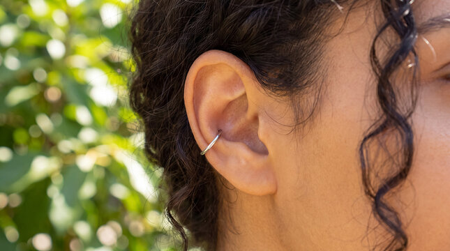 Person showing a pierced ear with a modern cuff earring, highlighting self expression and body adornment