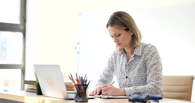 A dedicated professional is quietly engaged in her tasks at a contemporary office, surrounded by sunlight and vibrant stationery. The atmosphere is calm and productive.