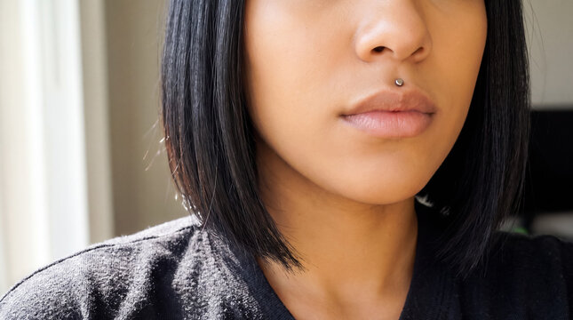 Young woman with short dark hair wearing a stylish philtrum piercing, representing individuality and modern beauty