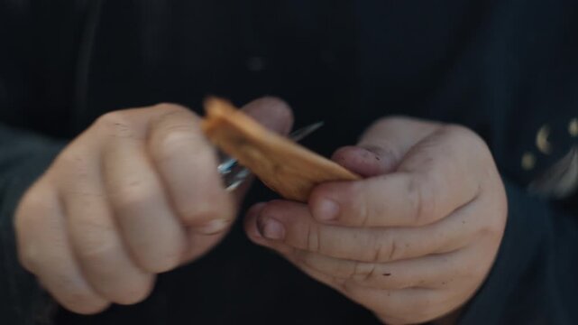 Toddler boy with dirty face cuts wood with little knife and enjoys making something by himself