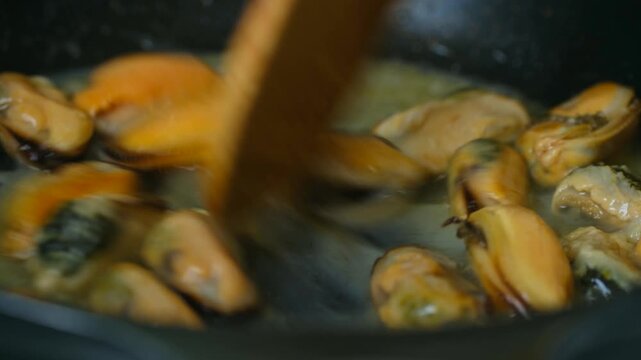 Delicious shelled mussels sizzling in a hot frying pan with bubbling butter or oil, being stirred with a wooden spoon during the cooking process for a tasty seafood recipe