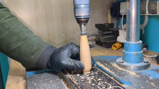 Gloved artisan applying liquid adhesive from a small cup onto a wooden handle, inserting a forged metal spoon component, and securing the assembly with a small metal pin fastener on workbench